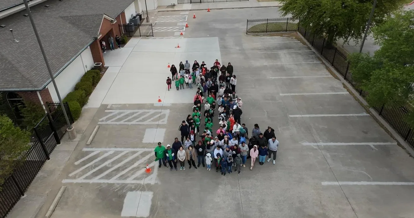 An aerial view of BASIS Plano students and families standing together in the school parking lot, arranged in the shape of a letter B