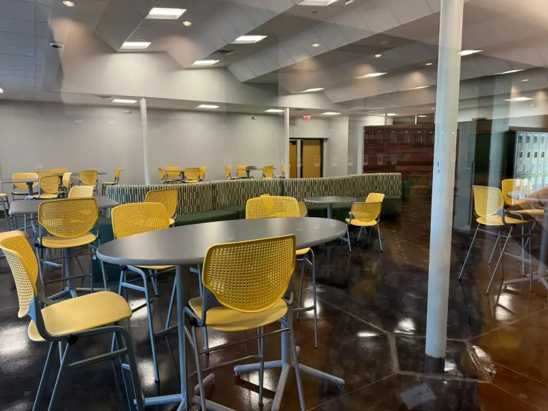 The student commons before opening, yellow stools pulled up to oval tables and a long banquette running along the wall