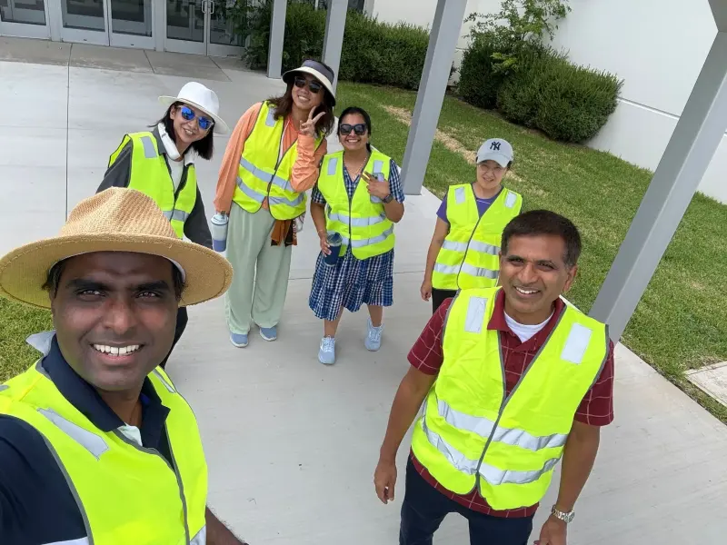 Six volunteers in hi-vis vests walking the path back from the drop-off lane, two waving at the camera
