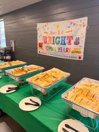 Four chafing trays of quesadillas lined up along the buffet under the bright-school-year banner, plates and tongs ready
