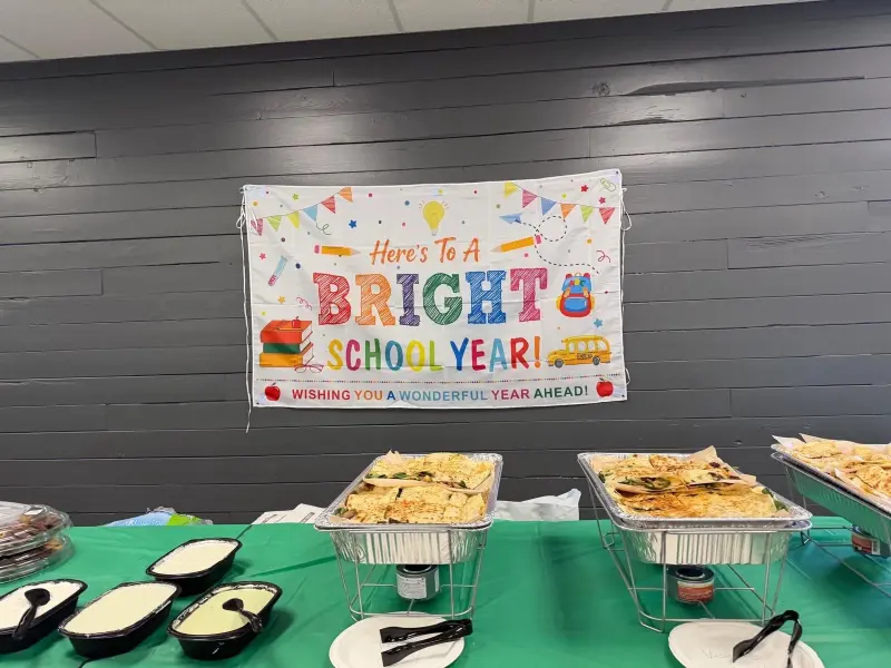 A “Here’s to a bright school year” banner hung on the dark panelled wall above the buffet, quesadillas warming in chafing trays below