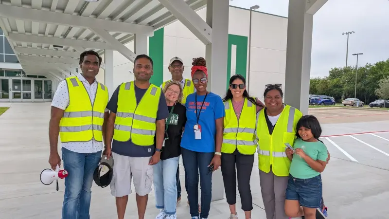 Nine carline volunteers in hi-vis vests and Booster shirts posing together under the canopy, one holding a megaphone