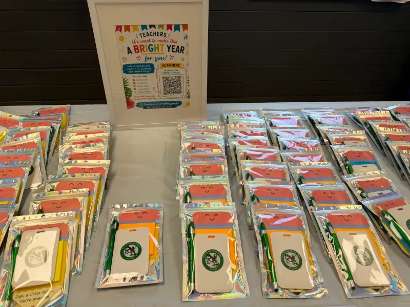 Dozens of wrapped gift packs laid out in rows, each with a husky-crest notebook and pen, beside a framed sign for teachers