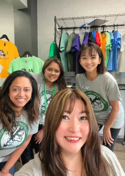 A selfie of four volunteers in Booster shirts in front of the rack of spirit wear