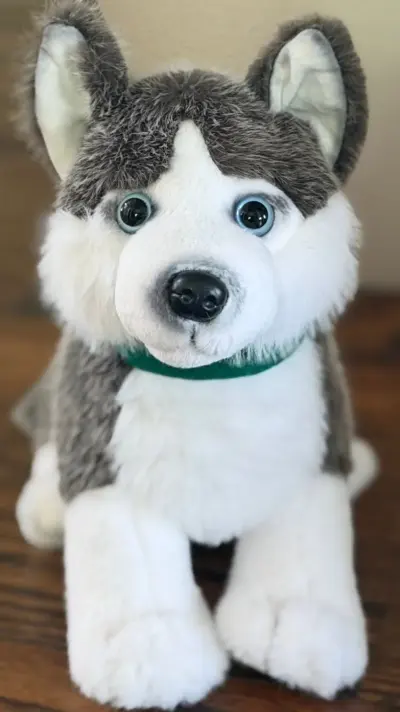 The husky plush close up on a wooden table, green bandana round its neck