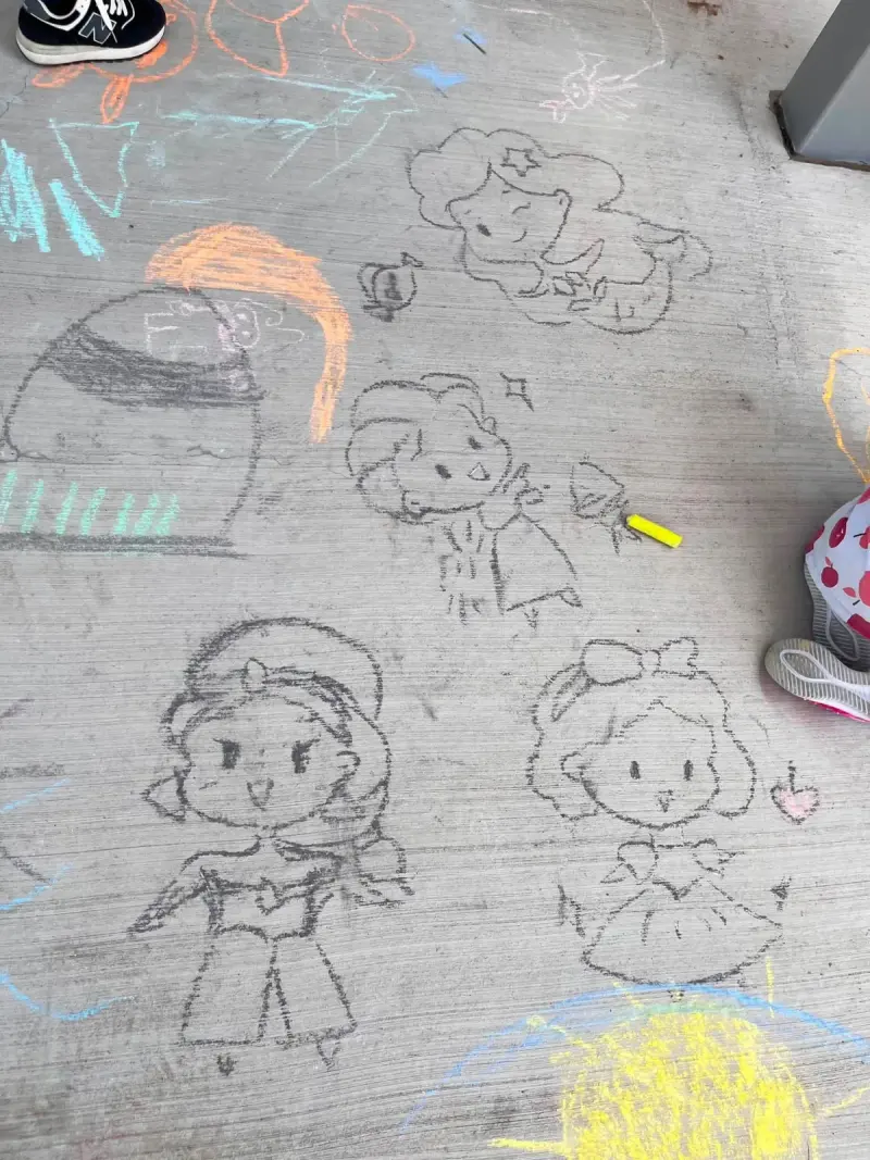 Chalk drawings of cartoon characters covering a slab of the walkway, children’s shoes at the edges of the frame