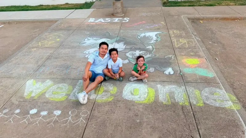A parent and two children sitting in the middle of the finished mural, “Welcome” chalked in yellow across the walkway