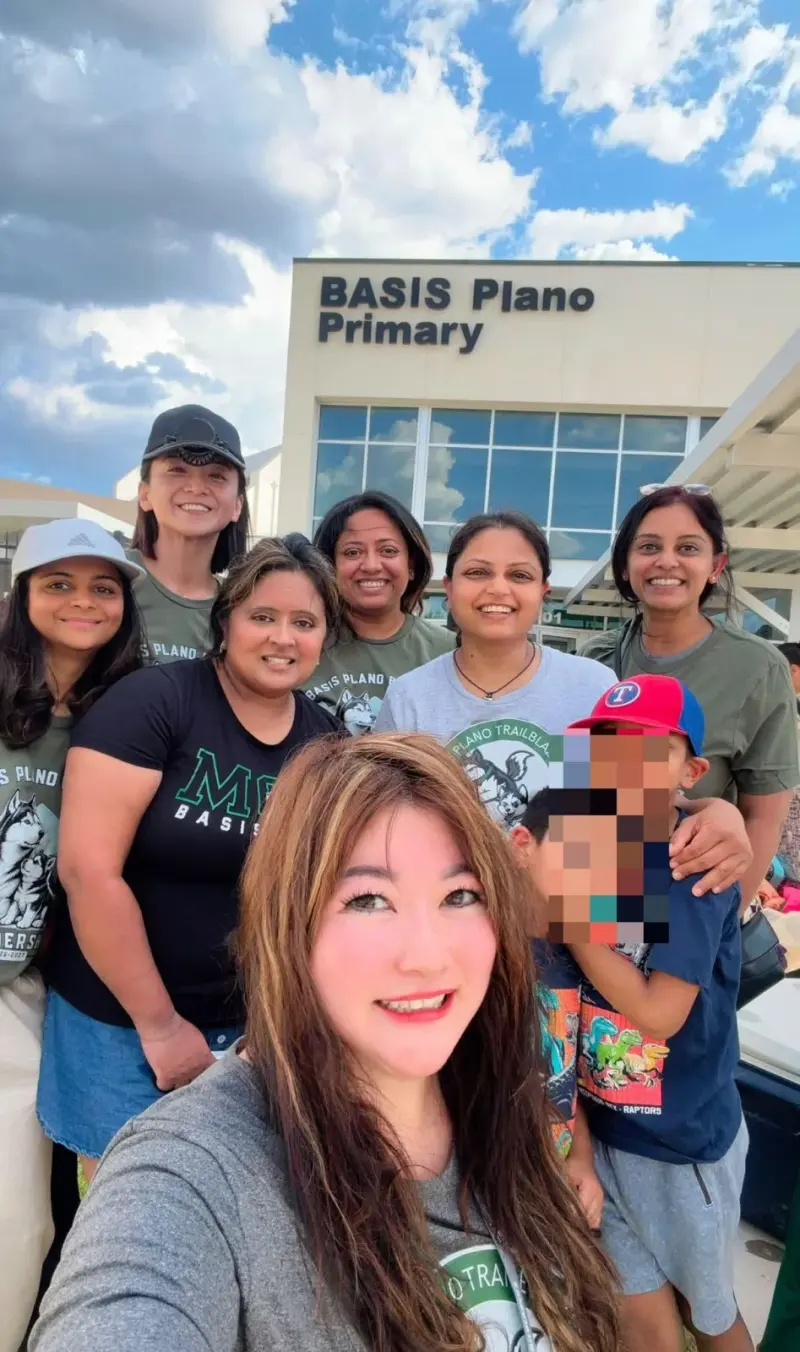 A selfie of seven volunteers and a child outside the Primary building under a bright cloudy sky