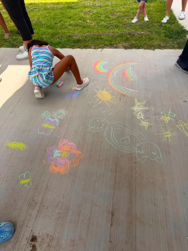 A child lying on the path to draw, a chalk rainbow, sun, stars and flowers covering the concrete around them