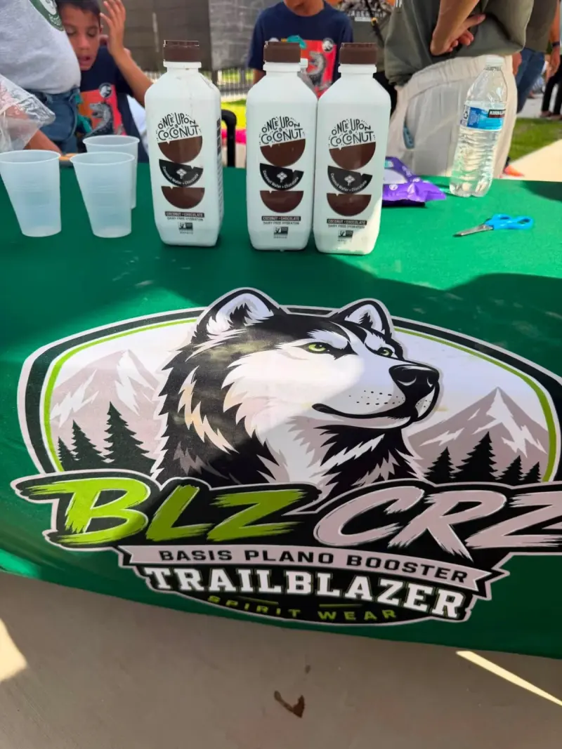 Bottles of chocolate coconut water and stacks of cups on the Booster tablecloth, children waiting at the end of the table