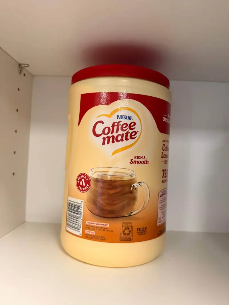A fresh tub of coffee creamer standing alone on an otherwise empty cupboard shelf