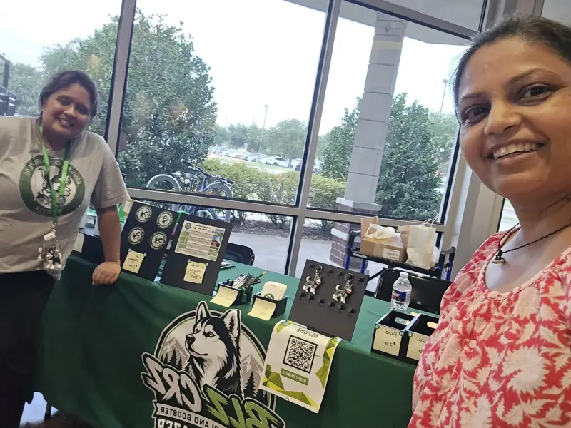 A volunteer behind the green Booster table, magnets, keychains and water bottles set out with handwritten price cards