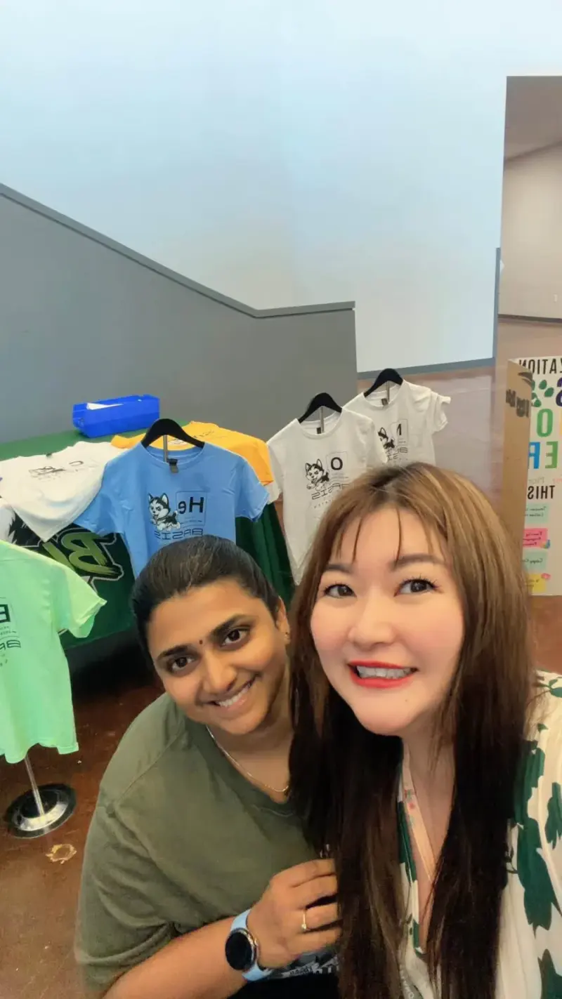 Two volunteers taking a selfie in front of the spirit wear stands at the end of the evening
