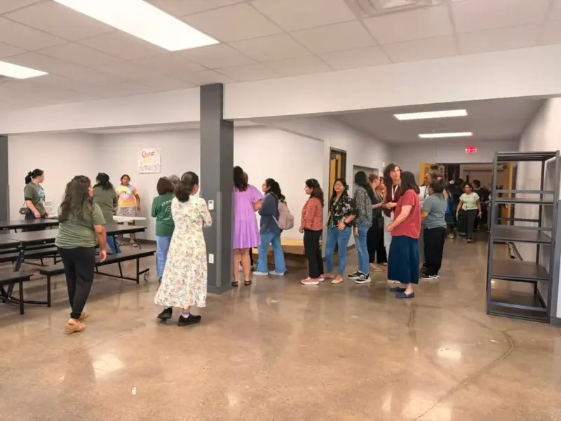 Staff queuing along the cafeteria wall for lunch, cafeteria benches folded up beside them