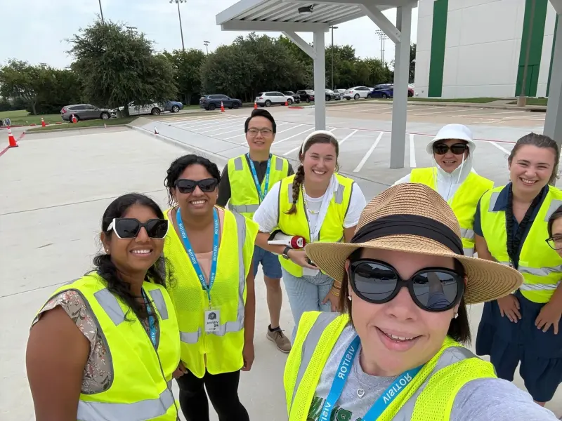 A selfie of seven carline volunteers in hi-vis vests under the pickup canopy, the car park behind them
