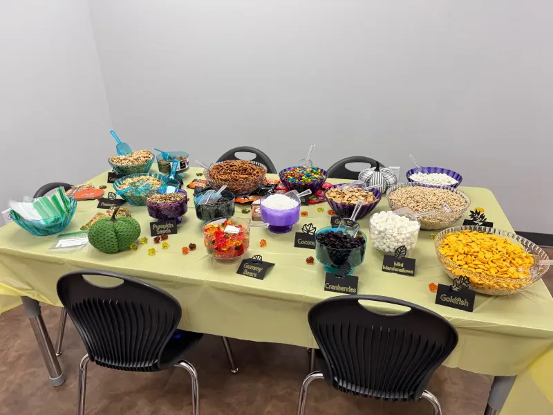 A long table laid with bowls of pretzels, nuts, dried fruit, marshmallows and sweets, each with its own labelled card