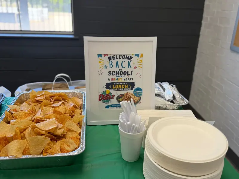A tray of tortilla chips and a stack of paper plates beside a sign thanking Dilla’s for donating the lunch