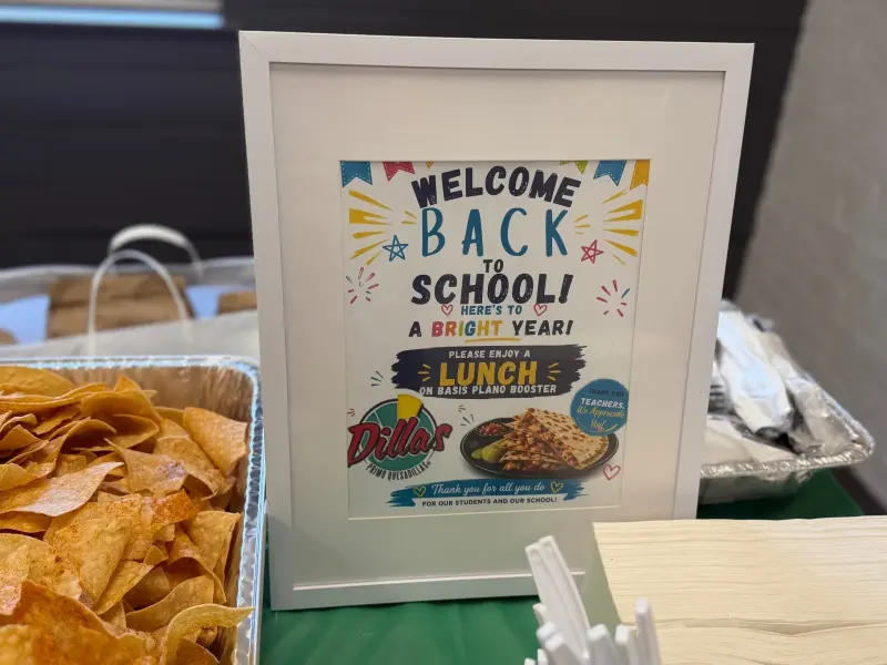 Close-up of the framed sign: “Welcome back to school — please enjoy a lunch on BASIS Plano Booster”, with the restaurant’s logo
