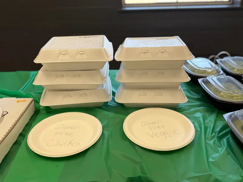 Stacked takeaway boxes behind two paper plates hand-labelled “gluten free chicken” and “gluten free veggie”