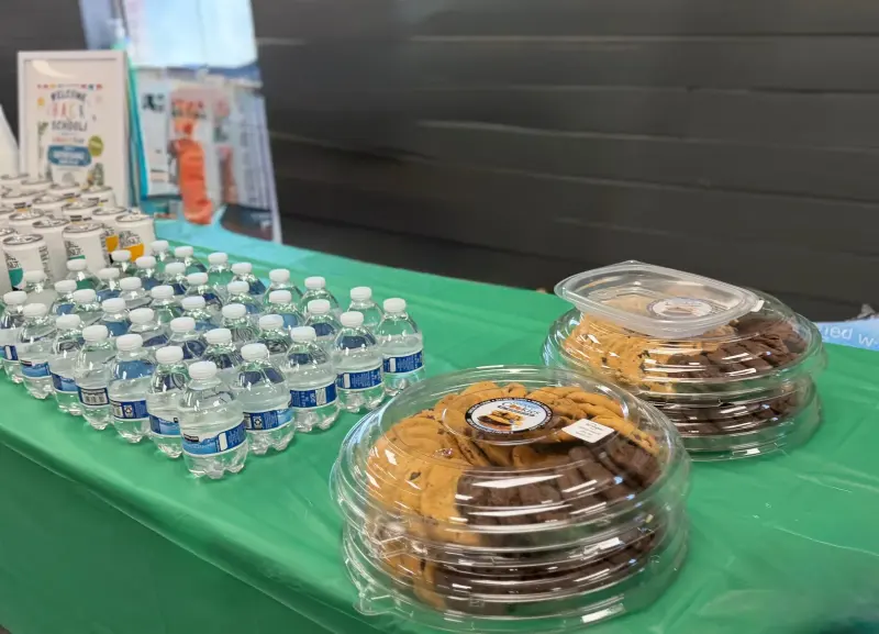 Platters of cookies under clear domes at the end of the table, rows of small water bottles beside them