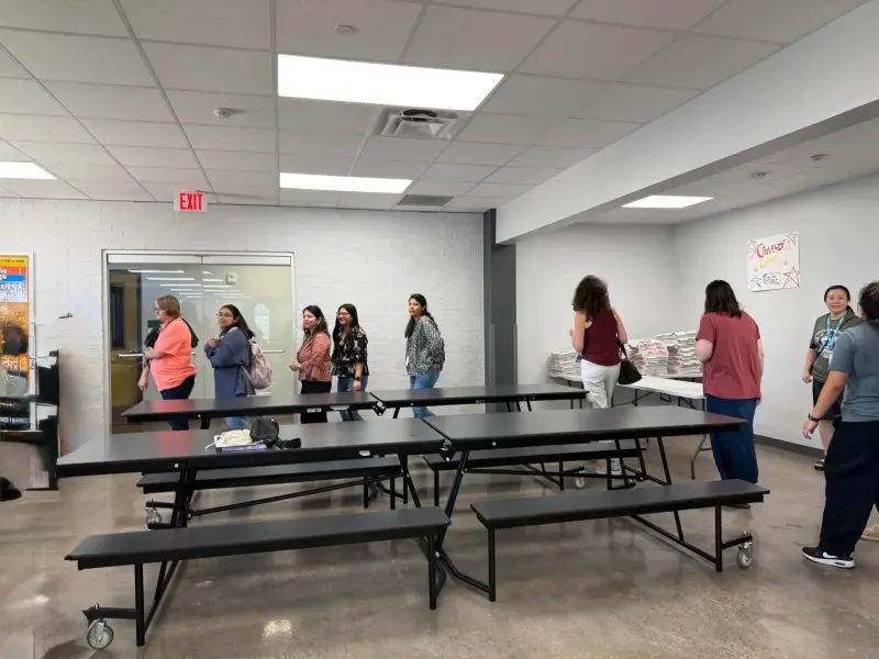 Staff crossing the cafeteria towards the gift table, folded bench tables in the foreground