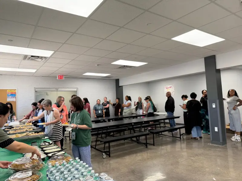 Staff working their way down the serving table while others wait along the wall, water bottles stacked at the near end