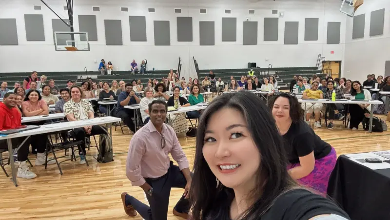 A selfie from the front of the gym looking back at the assembled teachers and staff seated at long tables