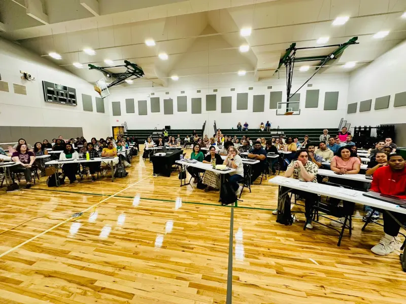 Staff seated at long tables set out across the gym floor for an opening-week session, bleachers folded back behind them