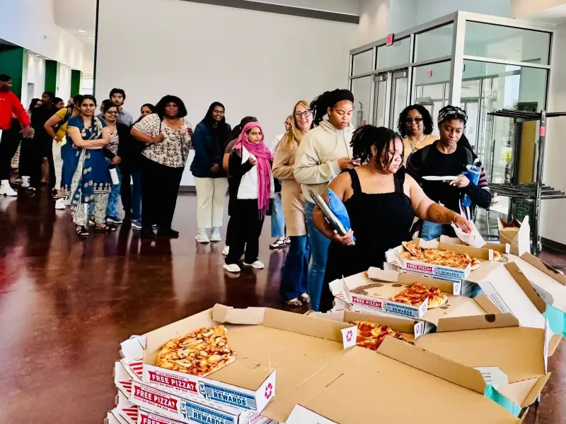 Staff queuing along the lobby past a long row of open pizza boxes laid out on a table