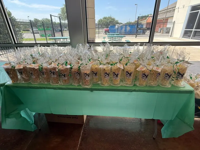 Dozens of cellophane-wrapped snack cups tied with green ribbon, lined up on a green-clothed table by the windows