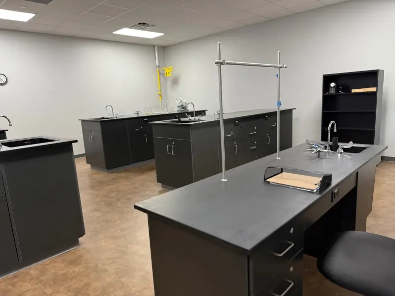 The science lab from the doorway, a fume-hood frame and ring stands on the near bench and eyewash station beyond