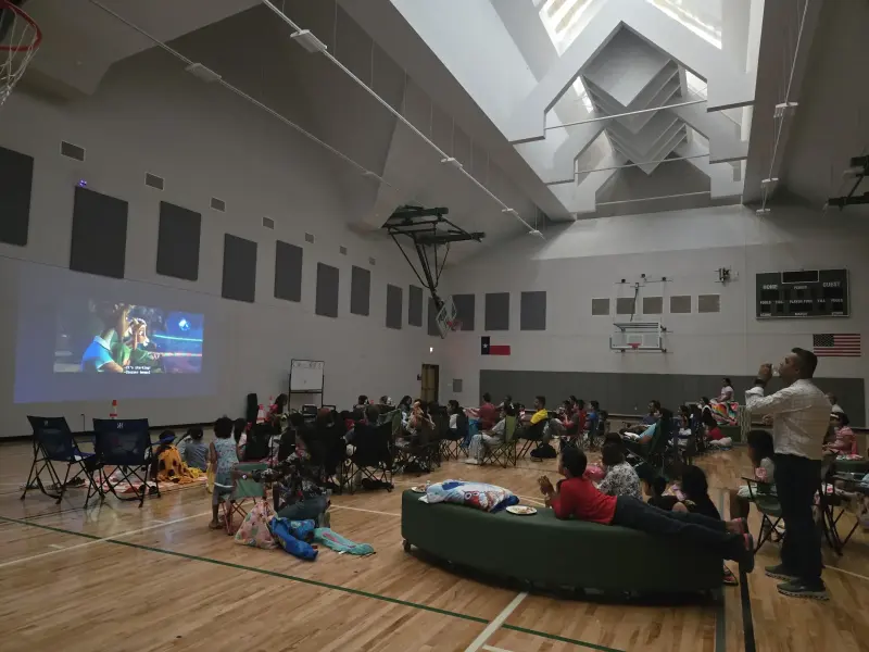 The film starting on the big screen at one end of the gym, families settled into camping chairs facing it