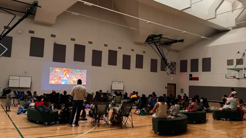Animated characters on the projected screen with families watching from chairs and benches across the gym floor