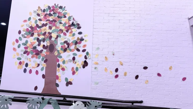 A painted tree on the wall with paper leaves spreading from its branches onto the white brick beside it