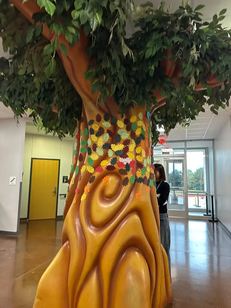 The lobby tree sculpture with paper leaves pinned up its trunk, a volunteer adding more at the side