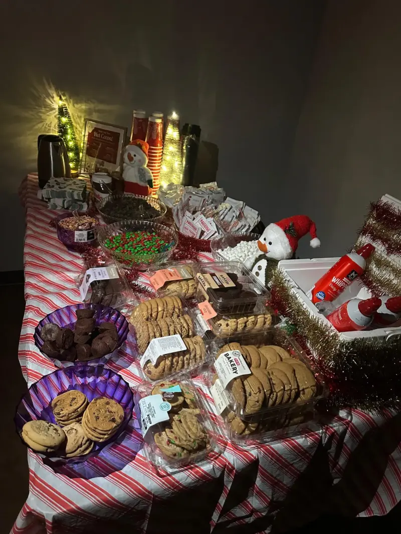 The cocoa bar by lamplight, trays of cookies and brownies laid out in front of the snowman and tinsel