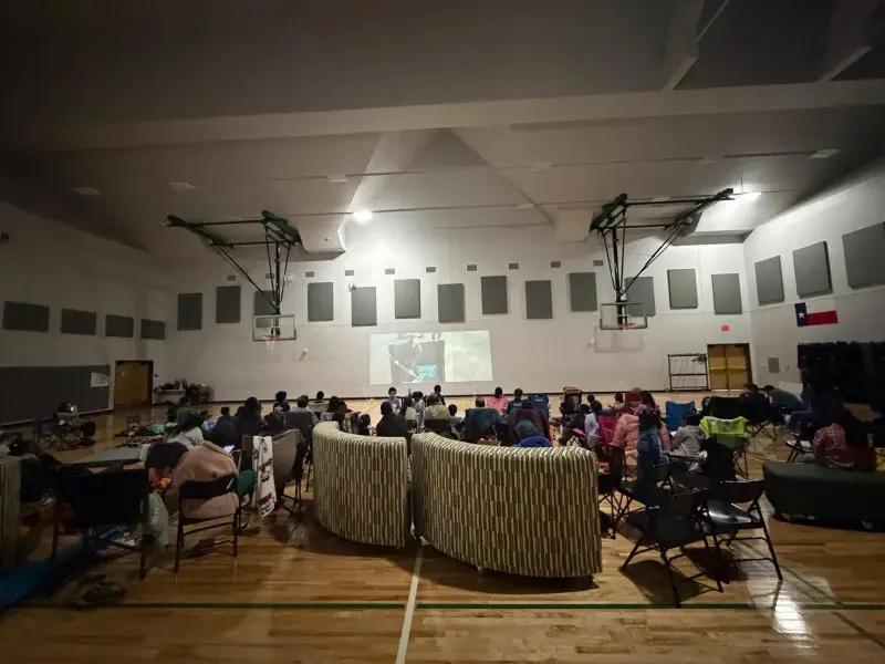 A wide view of the darkened gym, rows of chairs and a sofa pulled up in front of the screen