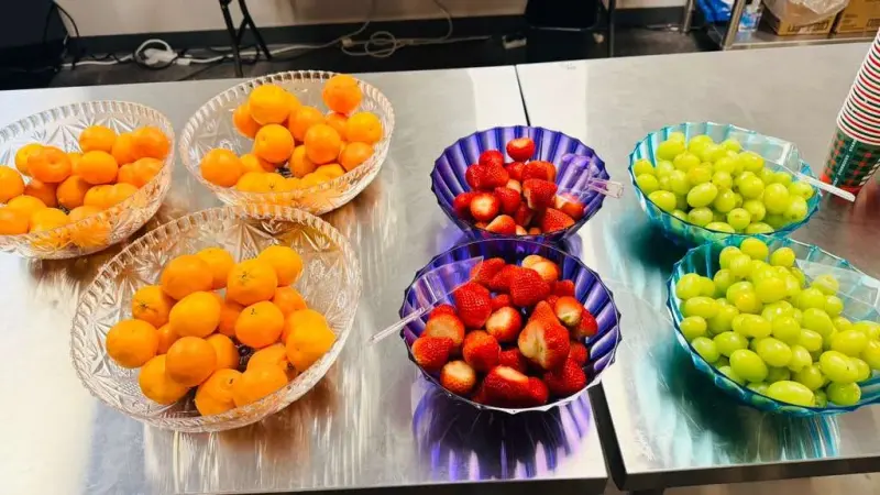 Cut-glass bowls of clementines, strawberries and green grapes lined up along a stainless counter