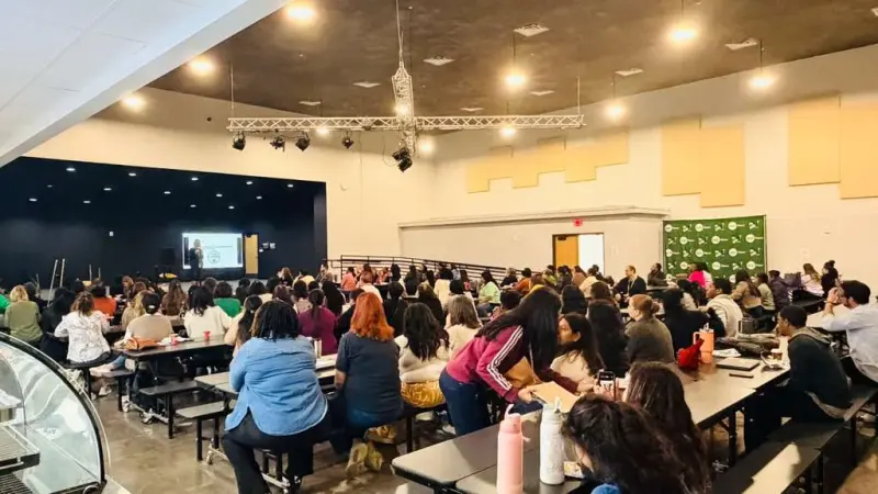 Teachers and staff filling the cafeteria tables for a morning session, a presentation on the screen at the front