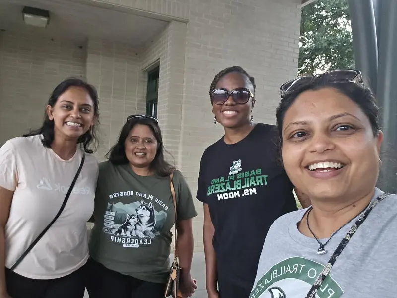 A selfie of four parents in Booster and Trailblazers shirts outside the school building