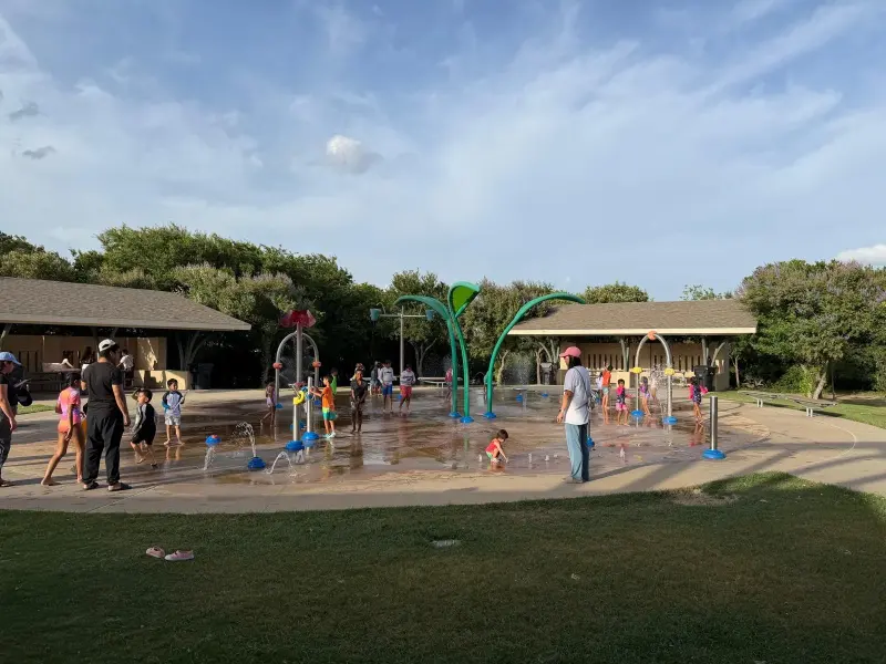 Children running through the sprays and hoops of the park splash pad on a bright afternoon