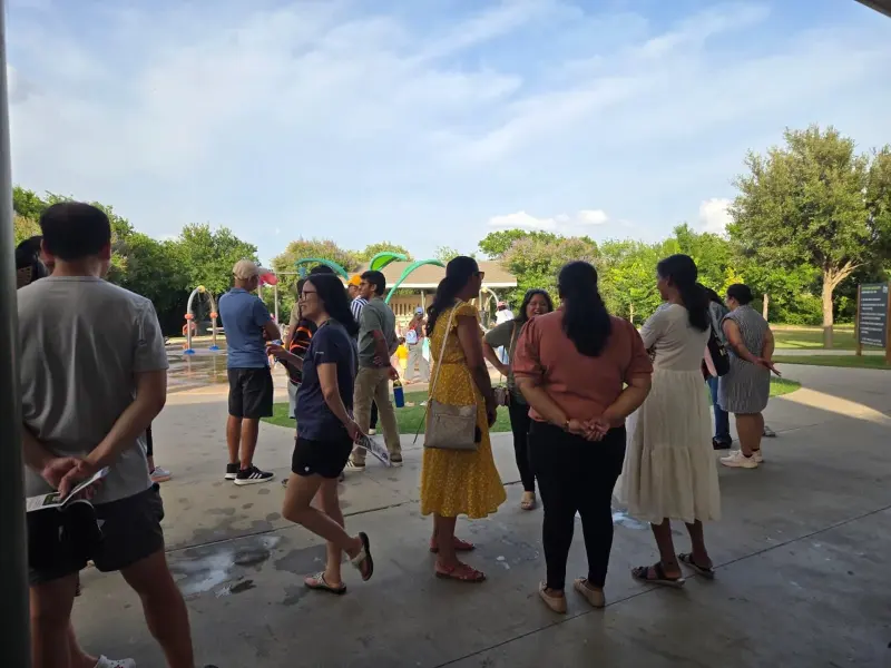Parents standing and chatting on the path beside the splash pad while the meetup gets going