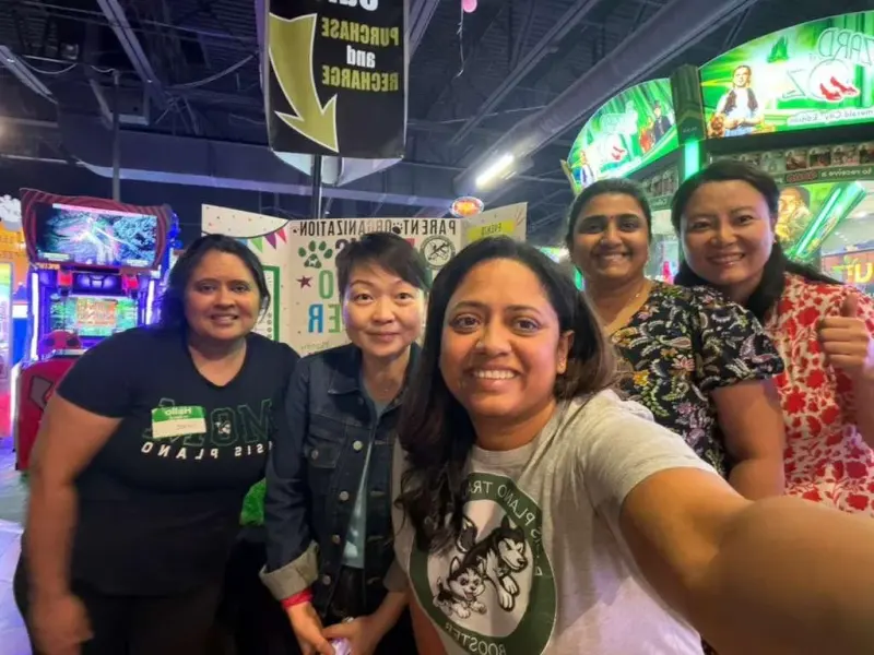 A selfie of five volunteers gathered in front of the Booster board under the arcade’s recharge sign