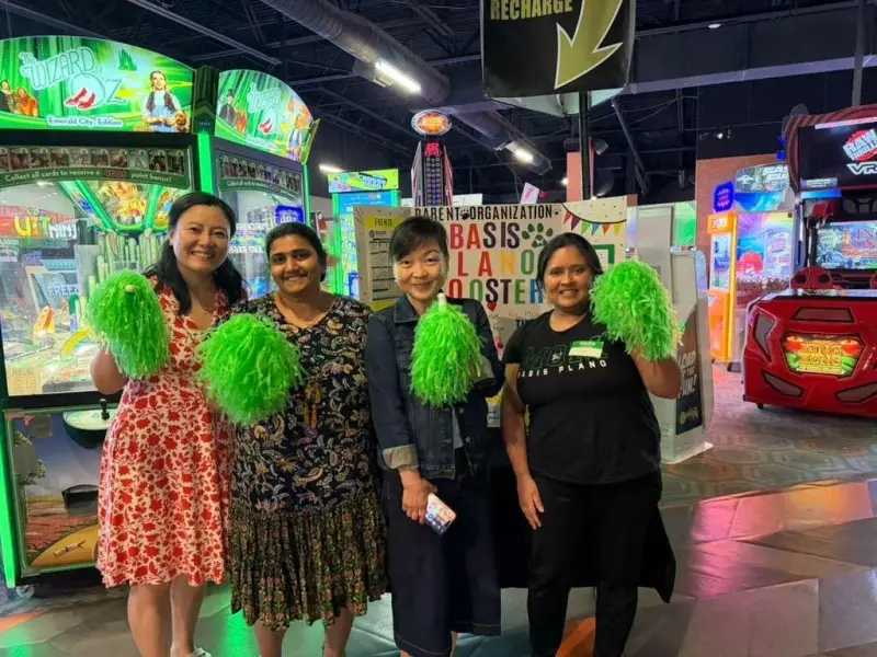 Four Booster volunteers holding up green pom-poms beneath the arcade’s recharge sign, the display board behind them