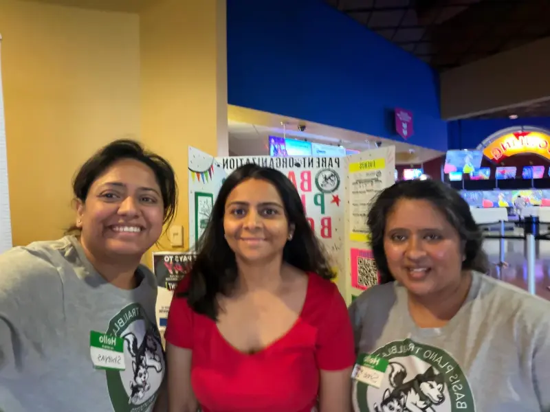 Three volunteers in matching Booster shirts in front of the display board, the bowling desk behind them