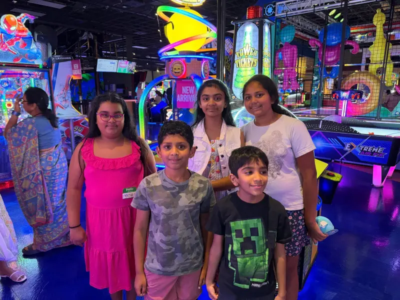 Five children lined up for a photo by the air hockey table, arcade lights and the play structure behind
