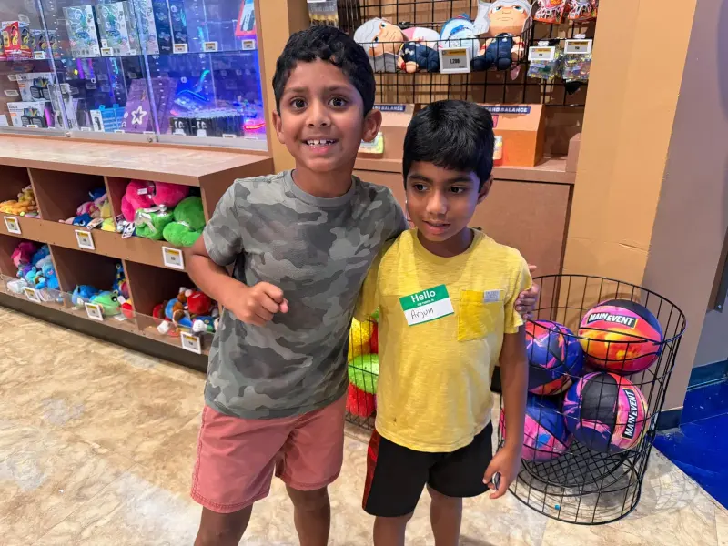 Two boys posing by the prize counter, the cubbies of soft toys and the redemption screens behind them